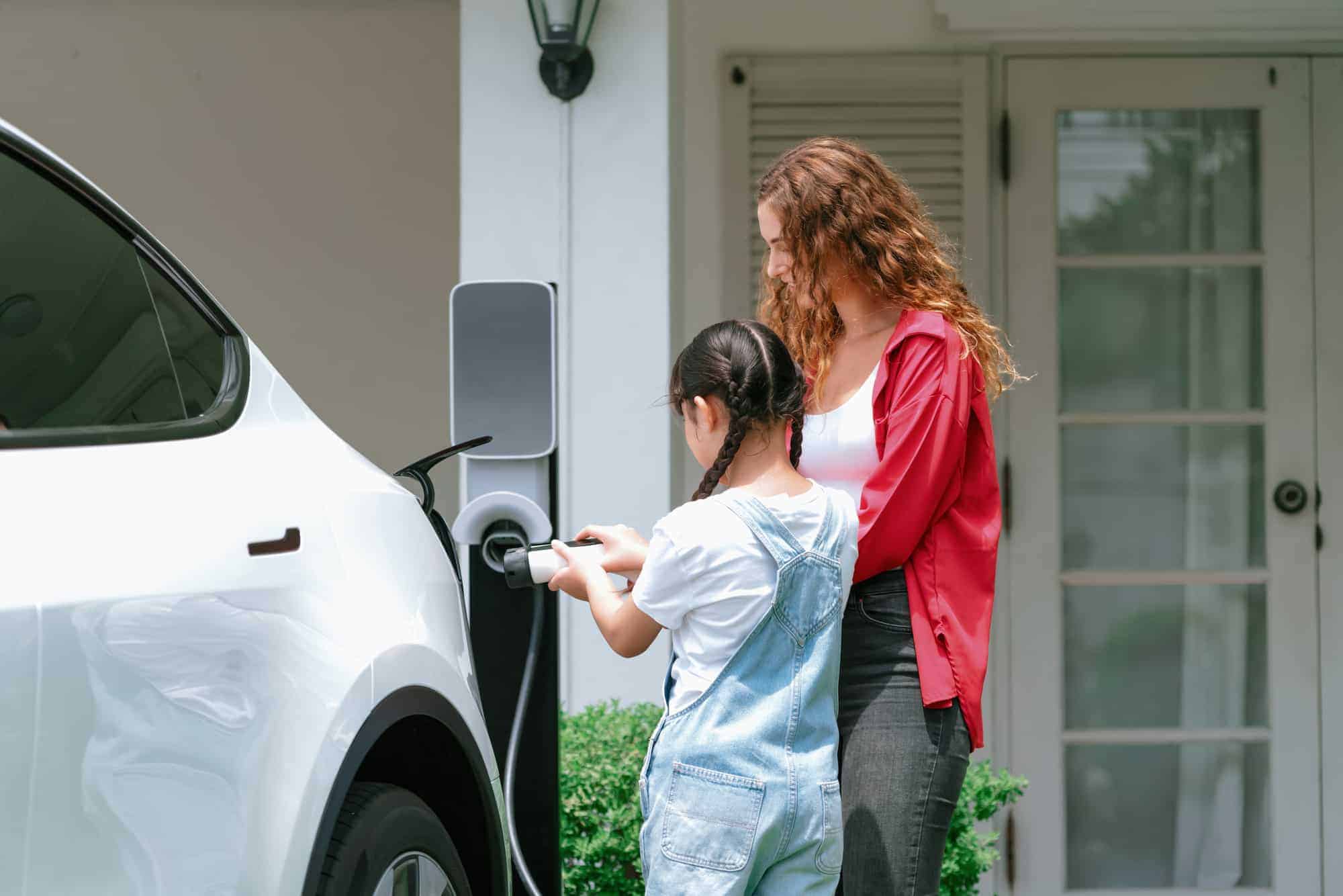 Photo d’une femme et d’une petite fille qui branchent une voiture électrique à une borne de recharge